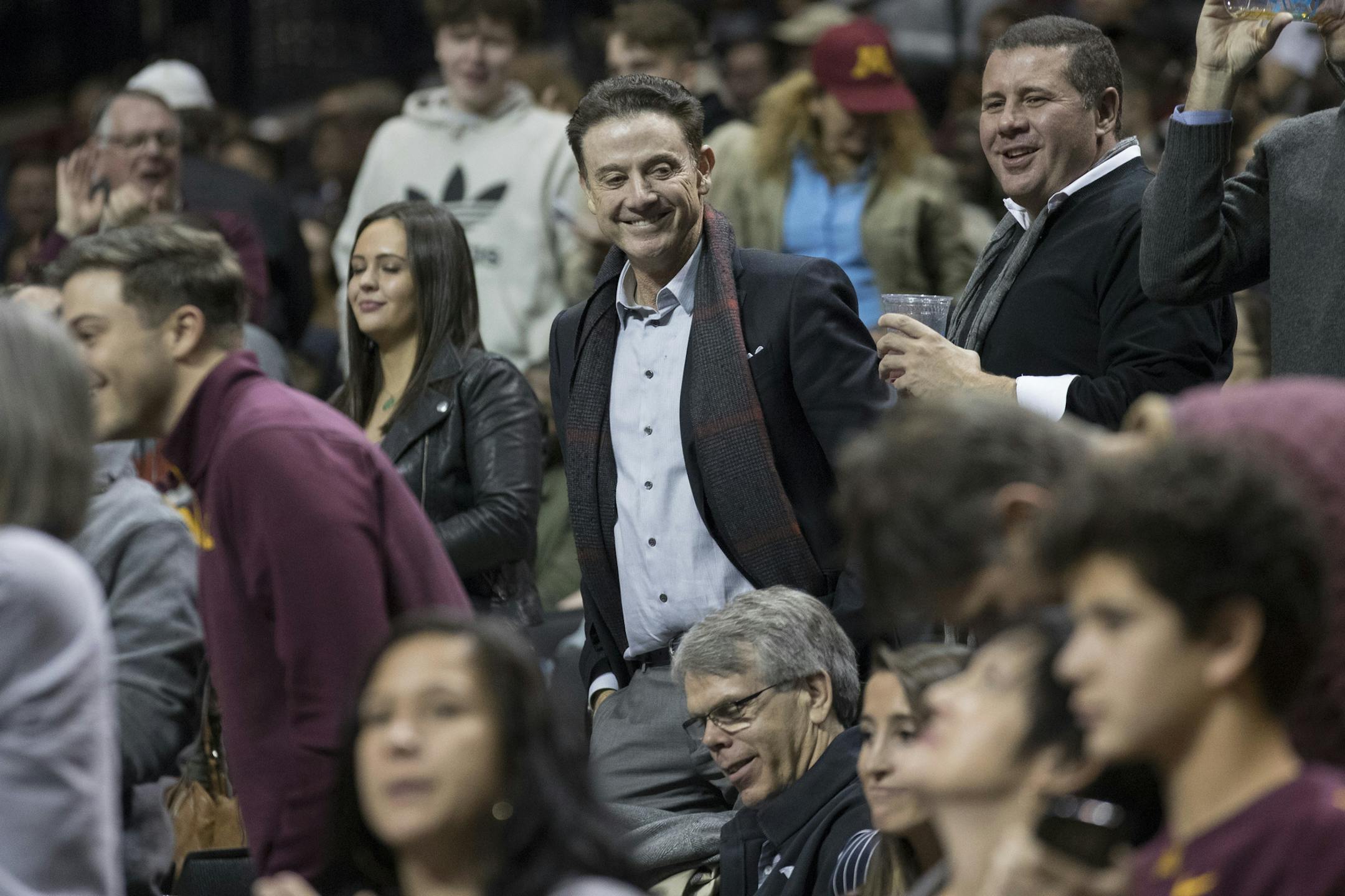 Former Louisville head coach Rick Pitino smiles as he watches the game action during the first half of an NCAA college basketball game between Alabama and Minnesota