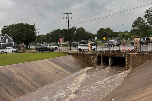 Water flowing through cement ditch with street in background and many vehicles parked.