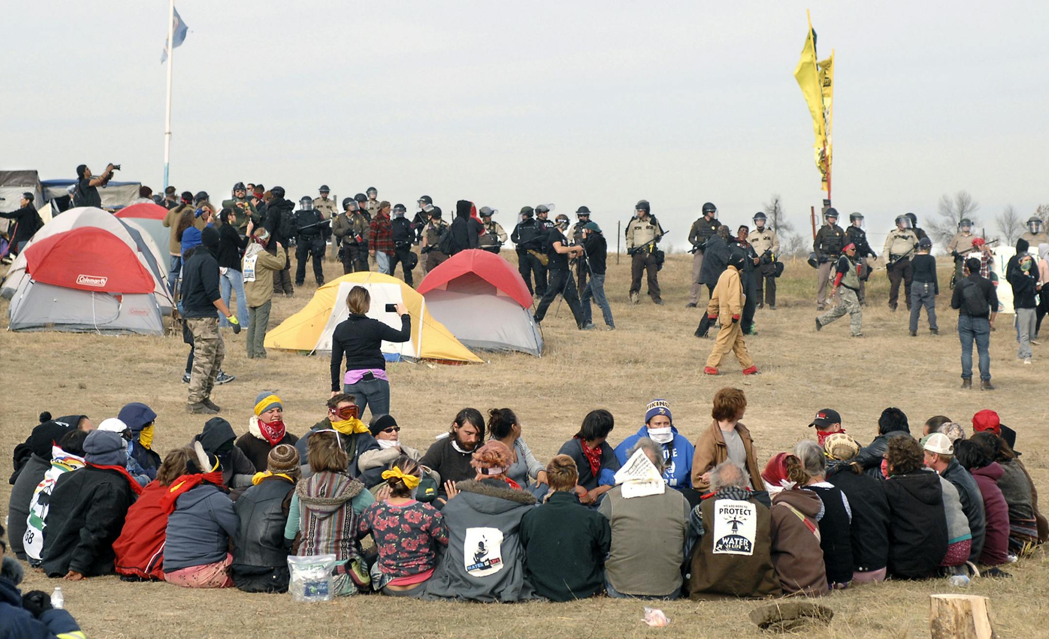 Dakota Access Pipeline protesters sit in a prayer circle Oct. 27 as a line of officers make their way across the camp to remove the protesters and relocate to the overflow camp a few miles to the south on Highway 1806 in Morton County, N.D.