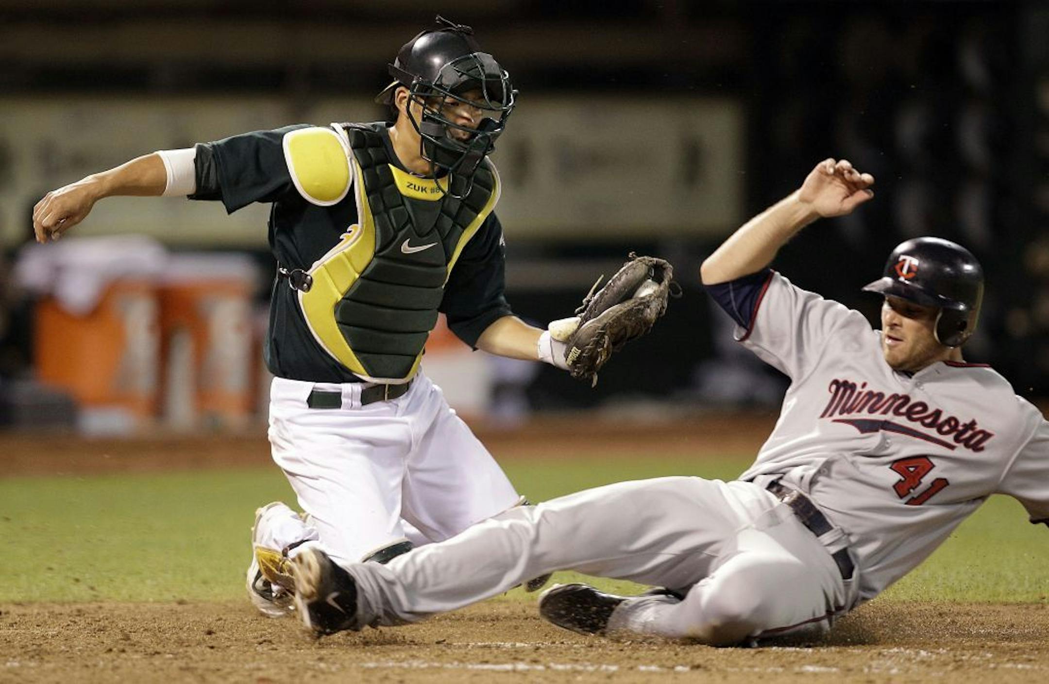Minnesota Twins' Drew Butera, right, scores as Oakland Athletics catcher Kurt Suzuki makes a late tag during the eighth inning of a baseball game Friday, July 29, 2011, in Oakland, Calif.