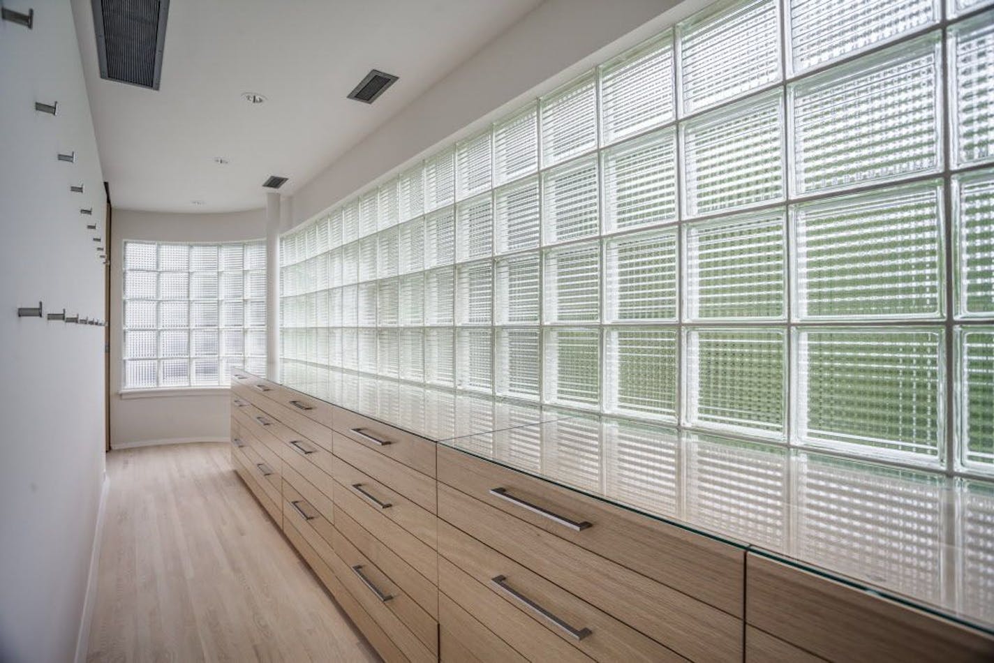 A large glass-block dressing room with a wall of storage drawers in the bedroom.