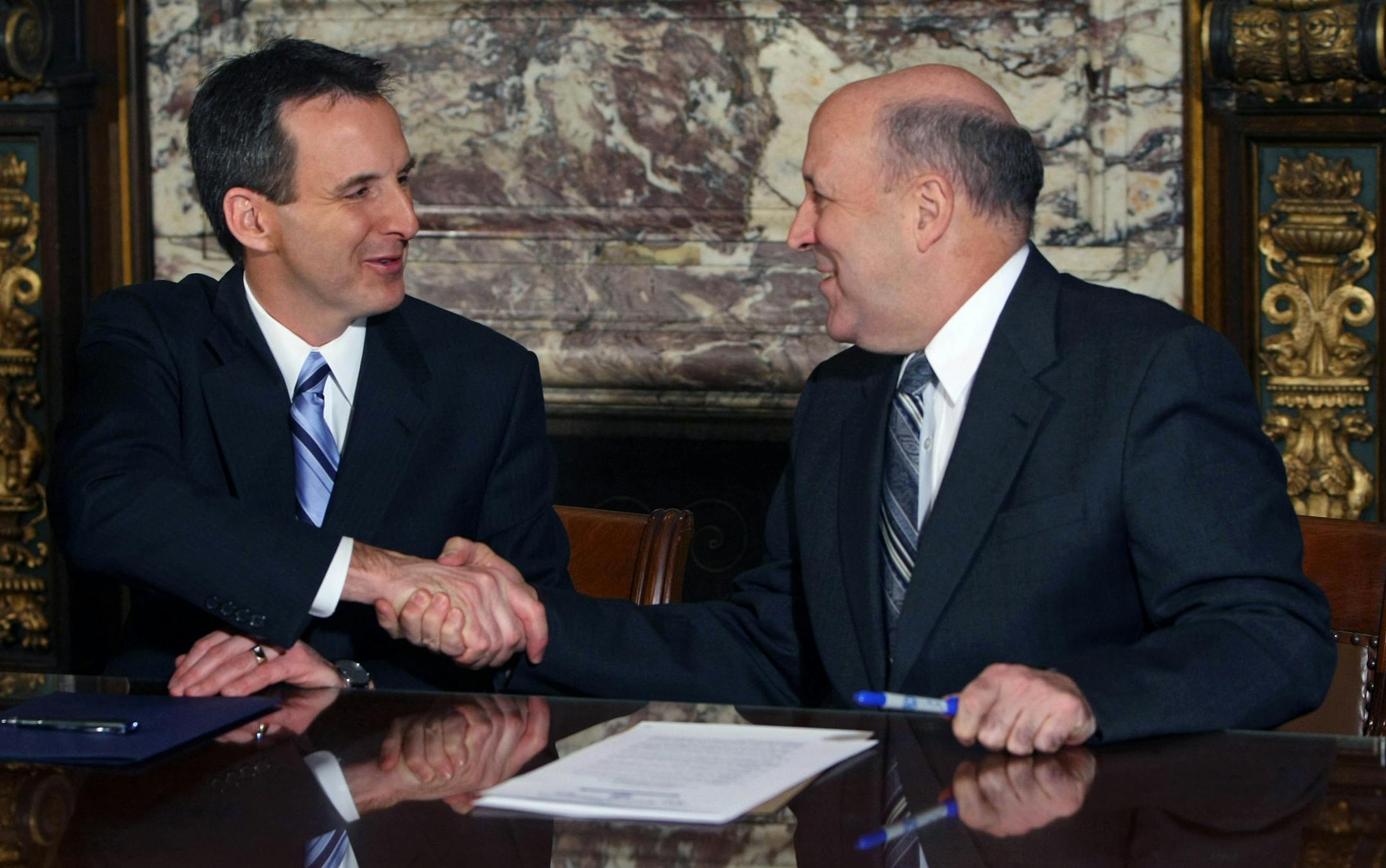 Gov. Tim Pawlenty, left, and Wisconsin Gov. Jim Doyle shook hands on Tuesday after signing executive orders directing their states to identify possible cooperative service agreements and cost savings.