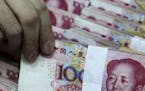 In this photo taken Tuesday, April 5, 2011, a clerk holds up a bundle of 100 yuan notes at a bank in Beijing, China. China's foreign reserves, by far 
