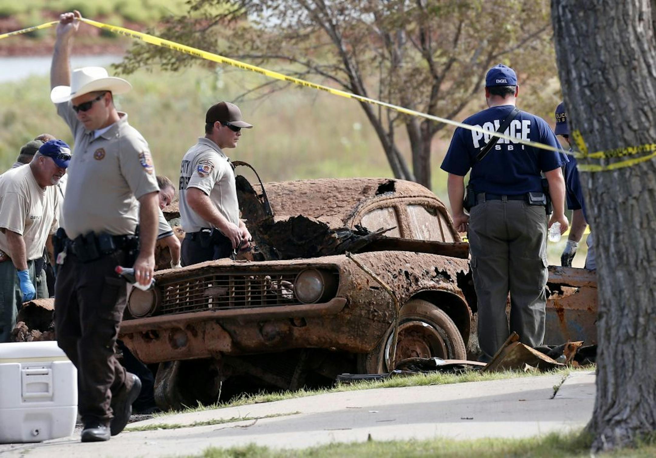 Law enforcement officials from multiple agencies examine the two cars pulled from Foss Lake, in Foss, Okla., Wednesday, Sept. 18, 2013.