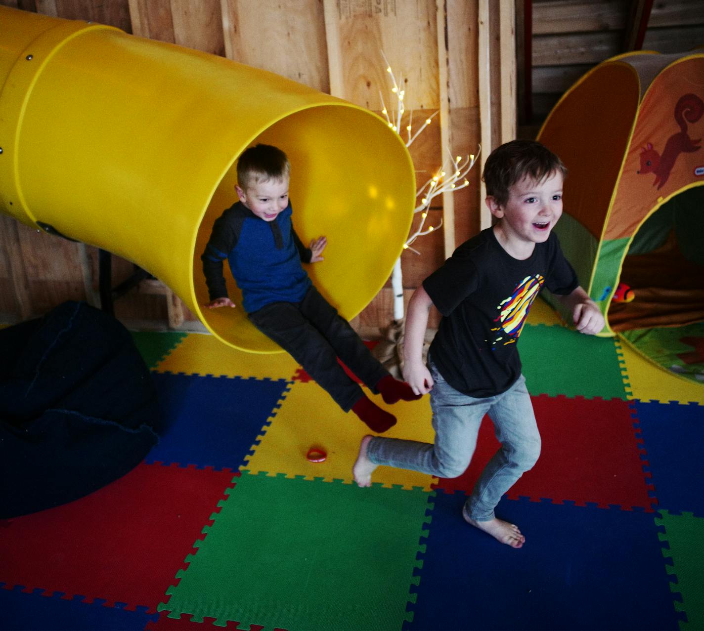 Leo Kuhl, 6, and his neighbor Elliot Budziak, 3, behind him, slide down the 30-foot-wide slide that descends from the first floor down to the basement.