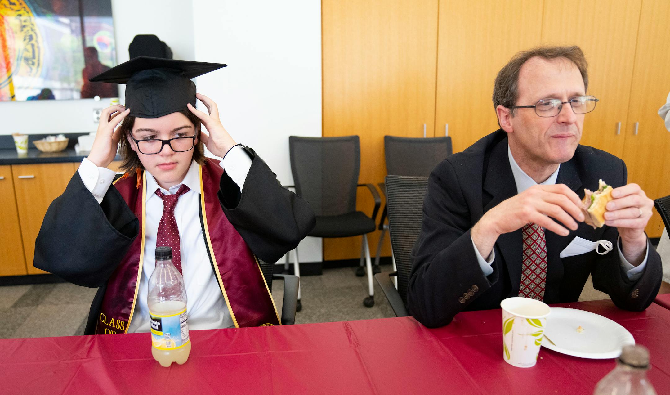 Elliott Tanner, 13, adjusts his graduation cap while sitting next to Paul Crowell, the head of the School of Physics and Astronomy, during a pre-graduation party.