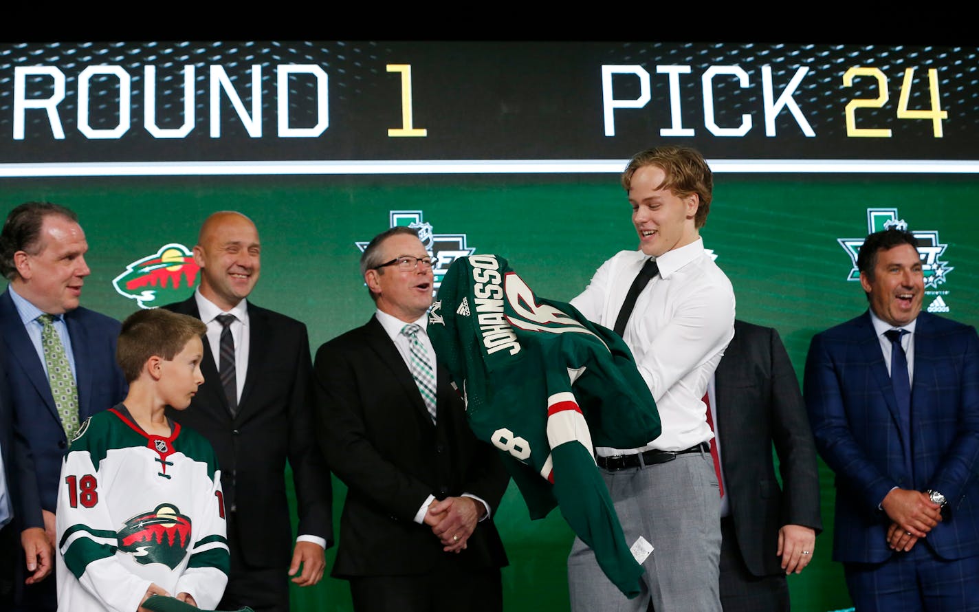 Filip Johansson, of Sweden, puts on a jersey after being selected by the Minnesota Wild during the NHL hockey draft in Dallas, Friday, June 22, 2018. (AP Photo/Michael Ainsworth)