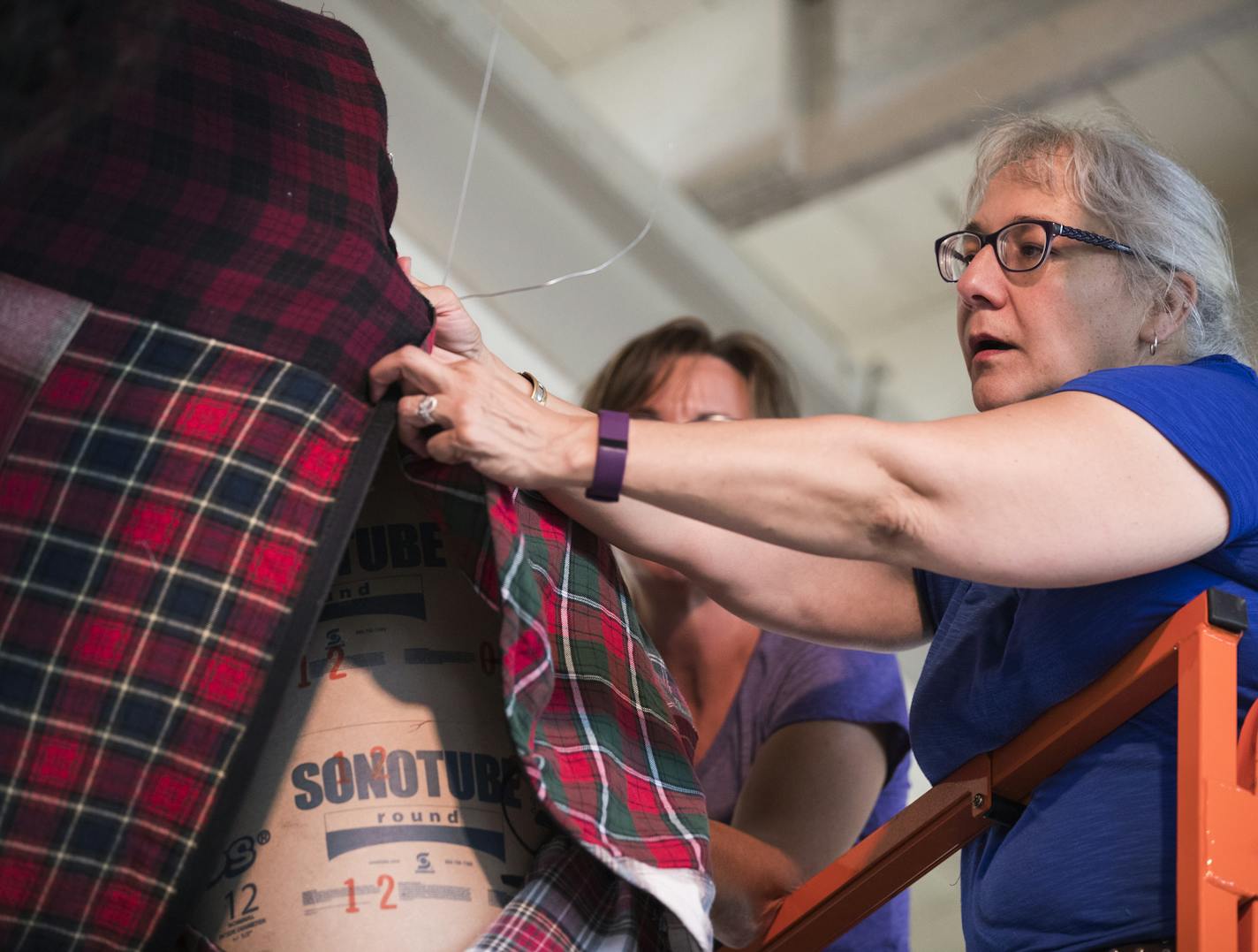 Alicia Wold of ReUse MN and CostumeRentals helps to fit Paul Bunyan into his shirt. Wold sewed the shirt using 40 flannel shirts, nine pairs of pajama pants, one skirt and one robe, all donated by Arc's Value Village. ] (Leila Navidi/Star Tribune) leila.navidi@startribune.com BACKGROUND INFORMATION: Inside the Eco Experience Building at the Minnesota State Fairgrounds in Falcon Heights on Thursday, August 18, 2016. The Minnesota Pollution Control Agency will unveil at the State Fair a 20 foot ta