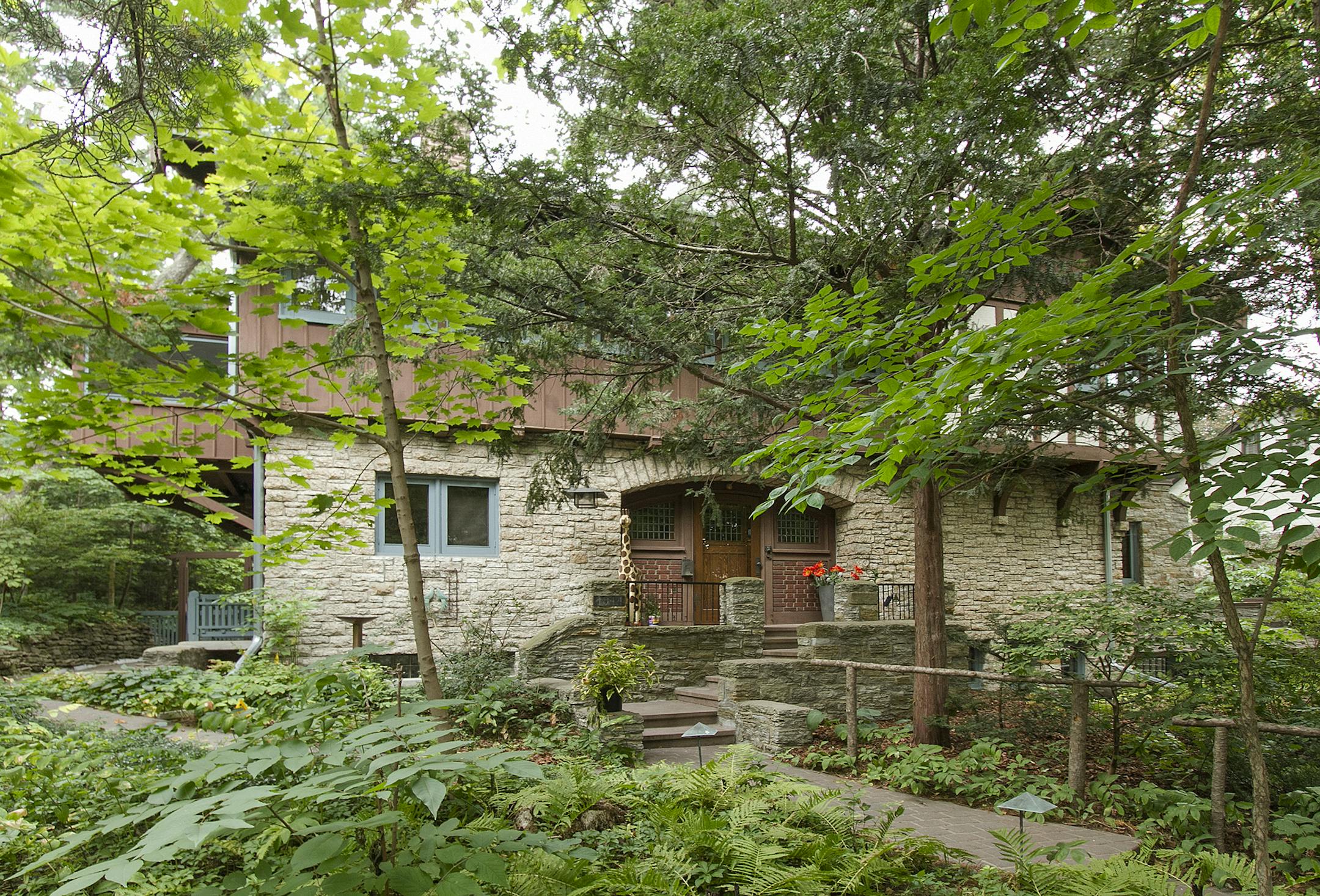 The stone-and-timber house is a blend of architectural styles that were popular in the early 20th century; it sits on a double wooded lot with trees planted by the original owner, a landscape architect.