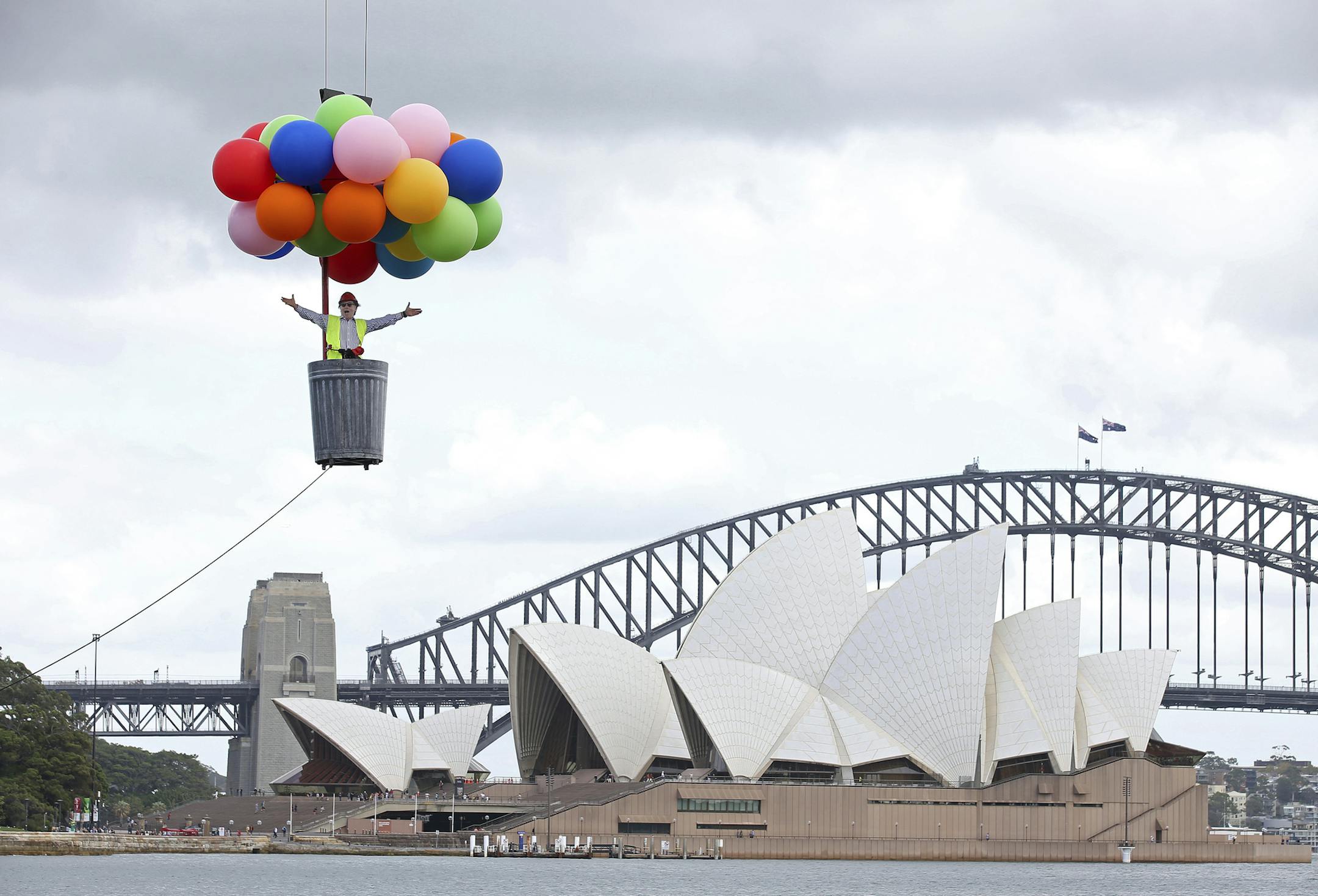 Opera Australia artistic director Lyndon Terracini rides in a garbage can under a balloon canopy over Sydney Harbour as he stands in for the character Parpignol during a test run of the prop for Puccini's La Boheme opera in Sydney, Tuesday, March 6, 2018. The production of La Boheme is set in a wintery 1960s Parisian landscape and opens on March 23. (AP Photo/Rick Rycroft) ORG XMIT: XRR101