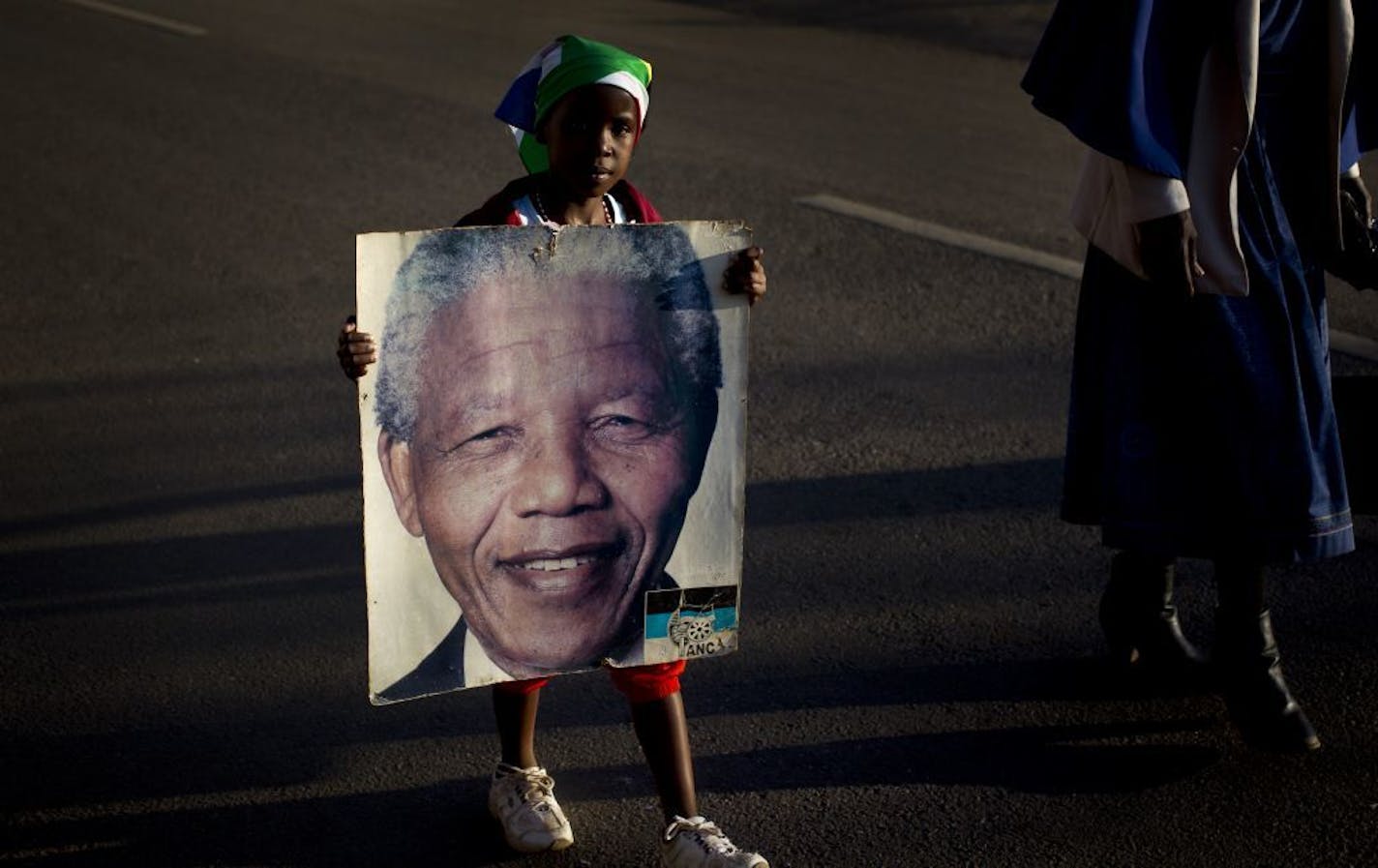 Lehlogonolo Nkosi, 7, holds a portrait of Nelson Mandela as she and her grandmother Florah, 52, right, leave after visiting the entrance where flowers and get-well messages have been left by well-wishers at the Mediclinic Heart Hospital where former South African President Nelson Mandela is being treated in Pretoria, South Africa Wednesday, July 3, 2013. A South African court ruled Wednesday that Nelson Mandela's grandson Mandla Mandela must return the bodies of the former president's three dece