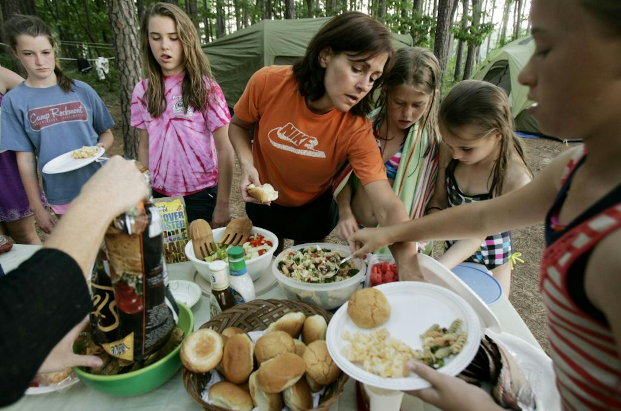 Dawn McNabb, center, helps serve dinner to Grace McCrorie, 13, far left, Jenna Laskowski, 13, Nora McNabb, 8, Rachel Laskowski, 9, and Grace McNabb, 11, far right, during an annual multiple family camping trip at Falls Lake Shinleaf Campground, June 10, 2011, in Raleigh, North Carolina. The families pre-make salads and casseroles to add to the meat that is grilled at the campground.