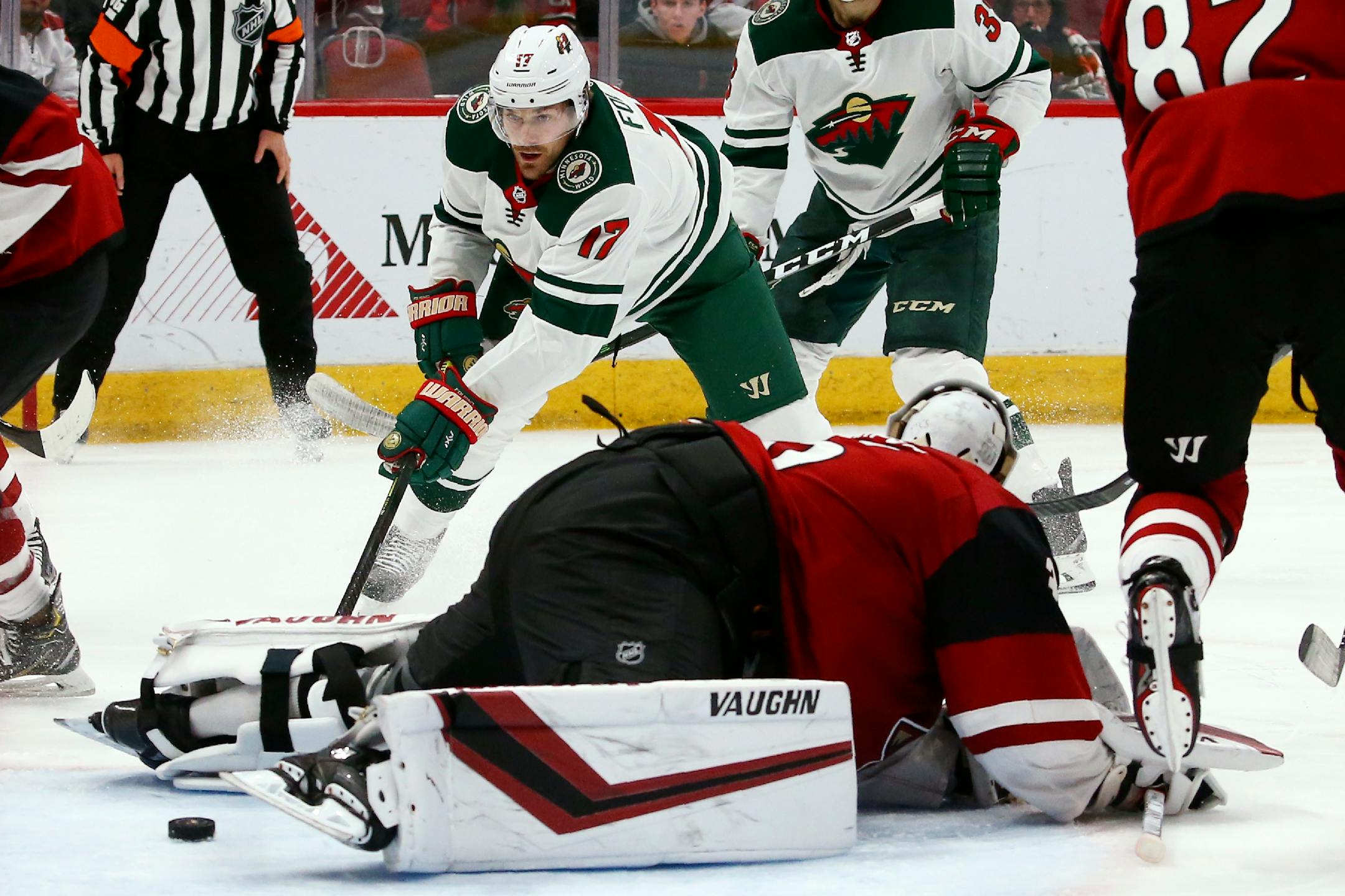 Arizona Coyotes goaltender Darcy Kuemper, front, stops the puck just enough to make a save on a shot by Minnesota Wild left wing Marcus Foligno (17) during the third period of an NHL hockey game Thursday, Dec. 19, 2019, in Glendale, Ariz. The Wild won 8-5. (AP Photo/Ross D. Franklin)