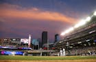 The setting sun reflects on storm clouds over the Minneapolis skyline and Target field as Minnesota Twins&#xed; Eddie Rosario comes to bat in a baseba