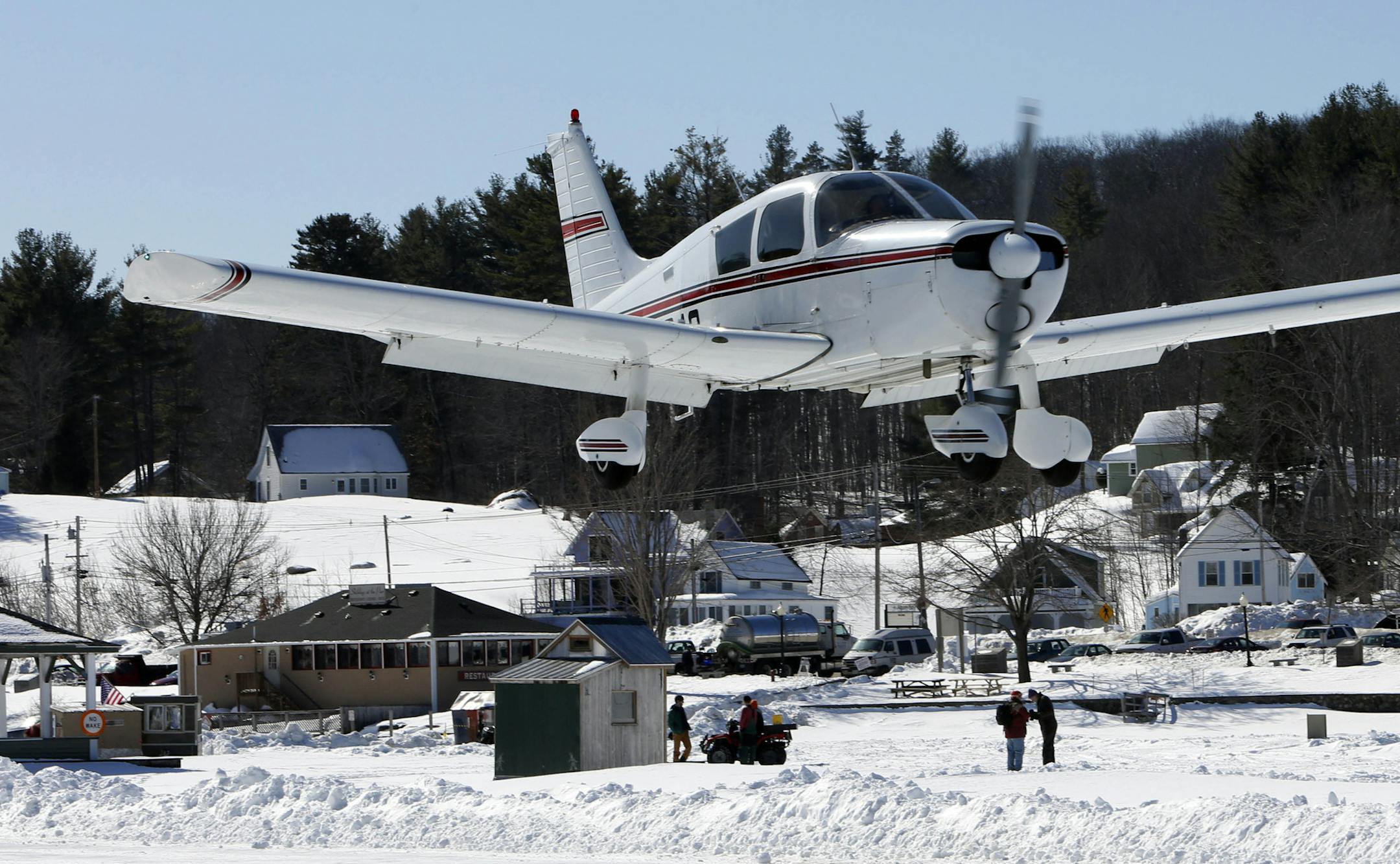 A plane flies in as ice fisherman fish on Lake Winnipesaukee Saturday, Feb. 28, 2015, in Alton, N.H. After weeks of bad weather the only ice runway in the Lower 48 states approved by the Federal Aviation Administration was open for fliers. (AP Photo/Jim Cole)