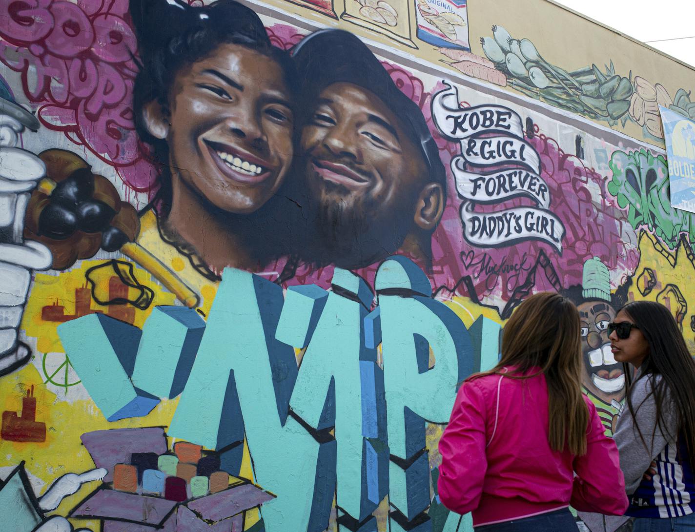 Kimberly Arellano and Abigail Tendrio pause in front of a mural put up of Kobe Bryant and his daughter along Pickford Street in Los Angeles, Monday, Jan. 27, 2020. Bryant, the 18-time NBA All-Star who won five championships and became one of the greatest basketball players of his generation during a 20-year career with the Los Angeles Lakers, died in a helicopter crash Sunday. (David Crane/The Orange County Register via AP)