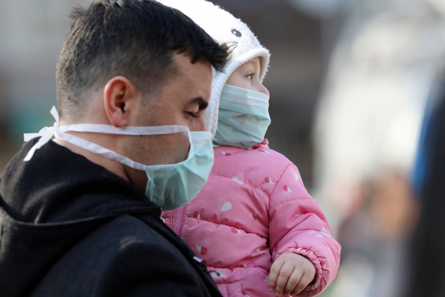 A man held a baby while walking by the entrance of Zekai Tahir Burak Hospital where 17 passengers of a Turkish Airlines flight from Tehran, suspected of having coronavirus, were to be quarantined, in Ankara, Turkey, Tuesday, Feb. 25, 2020. All 132 passengers of Tehran-Istanbul flight and crew on board will be quarantined for 14 days at the same hospital where Turkish citizens returning from China had been quarantined.( AP Photo/Burhan Ozbilici)