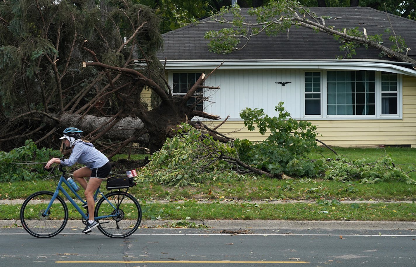 A woman rode her bike past a home with uprooted trees and storm damage after overnight storms with high winds rolled through the area in Richfield. ] ANTHONY SOUFFLE • anthony.souffle@startribune.com