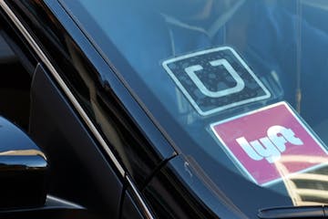 FILE - In this Tuesday, Jan. 12, 2016 file photo, a driver displaying Lyft and Uber stickers on his front windshield drops off a passenger in downtown