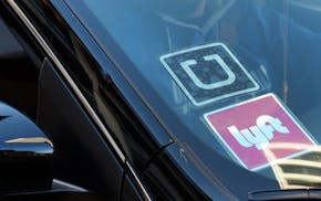 FILE - In this Tuesday, Jan. 12, 2016 file photo, a driver displaying Lyft and Uber stickers on his front windshield drops off a passenger in downtown