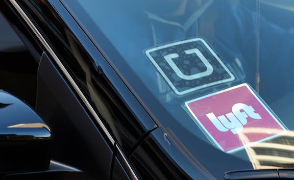 FILE - In this Tuesday, Jan. 12, 2016 file photo, a driver displaying Lyft and Uber stickers on his front windshield drops off a passenger in downtown