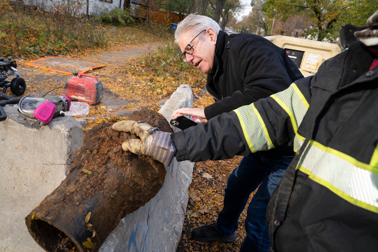 Nearby resident Jim Hagen takes a photo of a cast iron water main pipe from 1925 that utility workers cut off during the cleaning and lining process, showing the build-up inside, near 47th Ave S and Dowling Street in Minneapolis, Minn. on Friday, Nov. 3, 2023. ] LEILA NAVIDI • leila.navidi@startribune.com