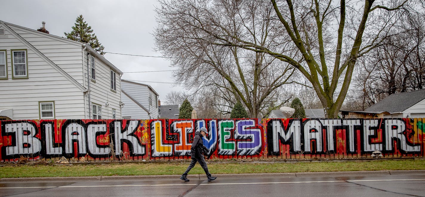 A man walks on the road near a fence that is at the center of controversy where a couple has been pressured by the City of West St. Paul to paint over their fence, Friday, April 9, 2021 in West St. Paul, MN. ] ELIZABETH FLORES • liz.flores@startribune.com