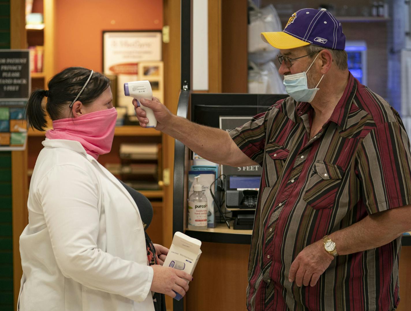 Heather Wingate helped Ronald W. Hildebrandt test his handheld thermometer inside the pharmacy in Baudette, Minn. on Thursday.