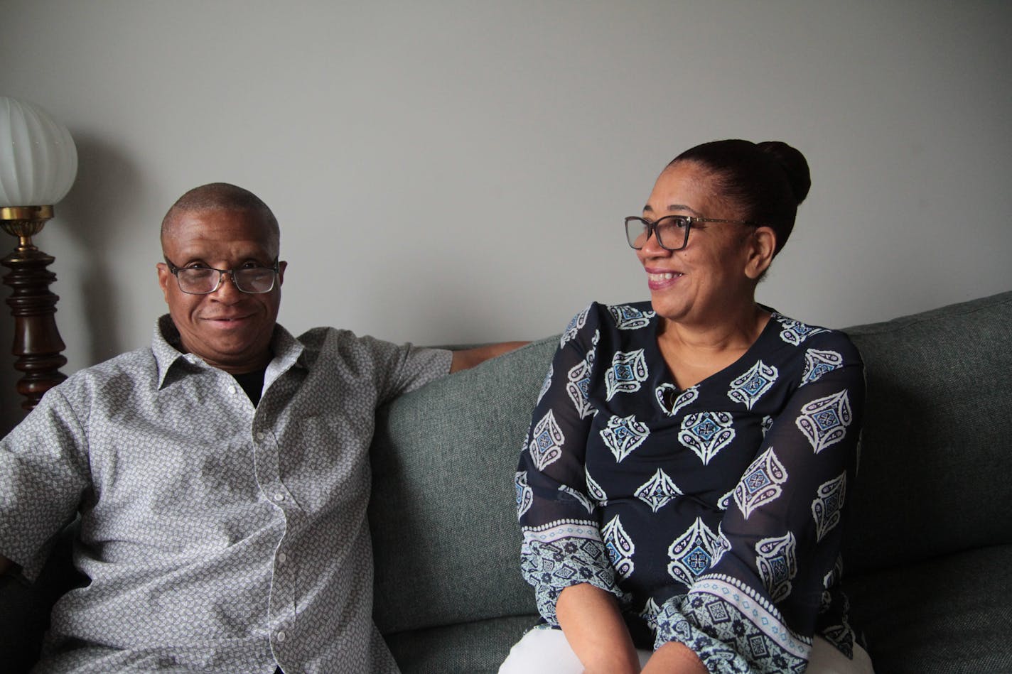 Larry Houston, a formerly homeless veteran, smiles on the couch in his new apartment. Hennepin County social worker Jeanetta Lindo, who specializes in finding housing for unhoused veterans, sits beside him and smiles.