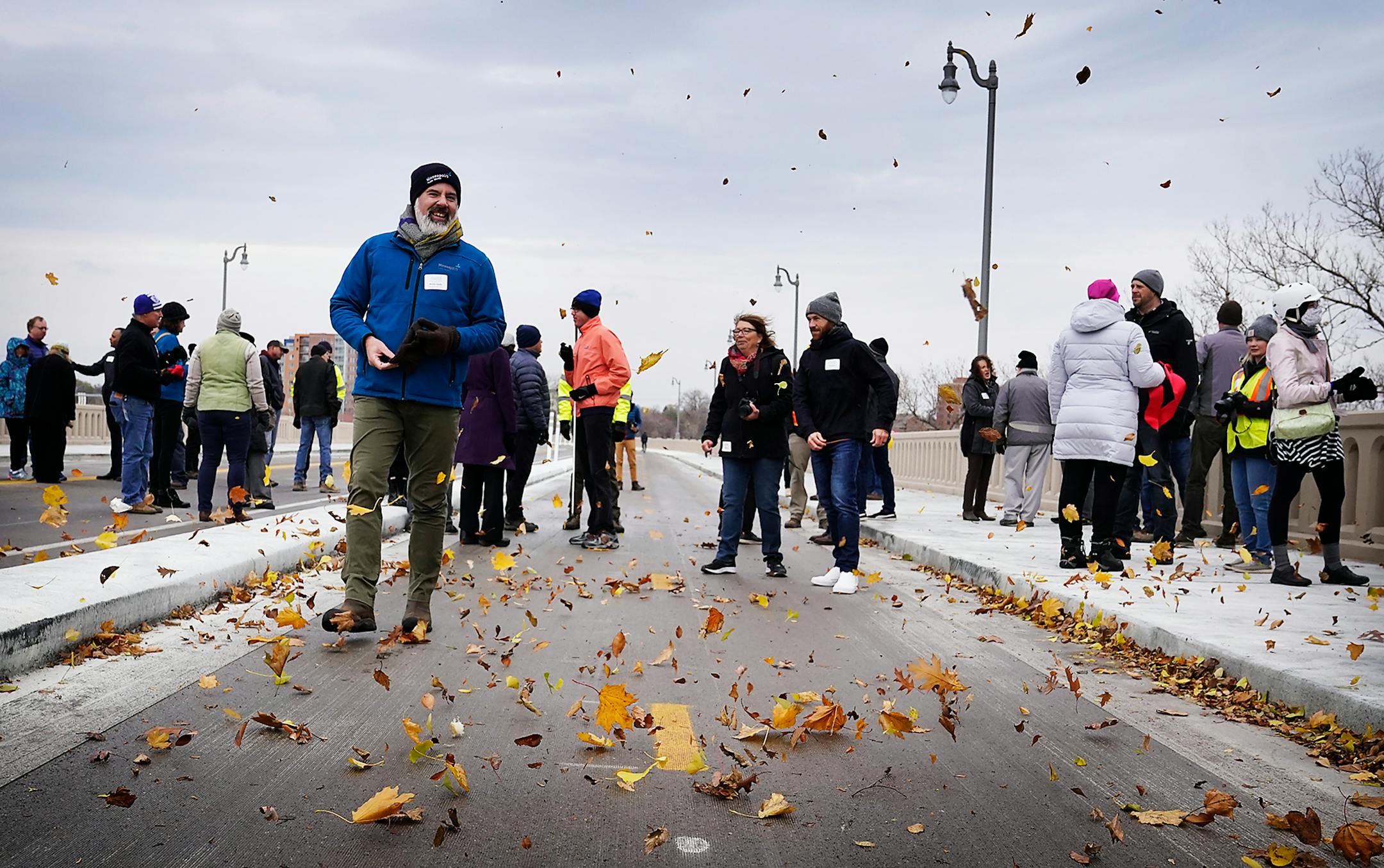 Leaves blow around, whipped up by high winds as people walk along the 10th Avenue Bridge after an official reopening ceremony Tuesday, Nov. 16, 2021 in Minneapolis, Minn. The 1929-era bridge over the Mississippi River has been rehabilitated and a new water main relocated under the river.]