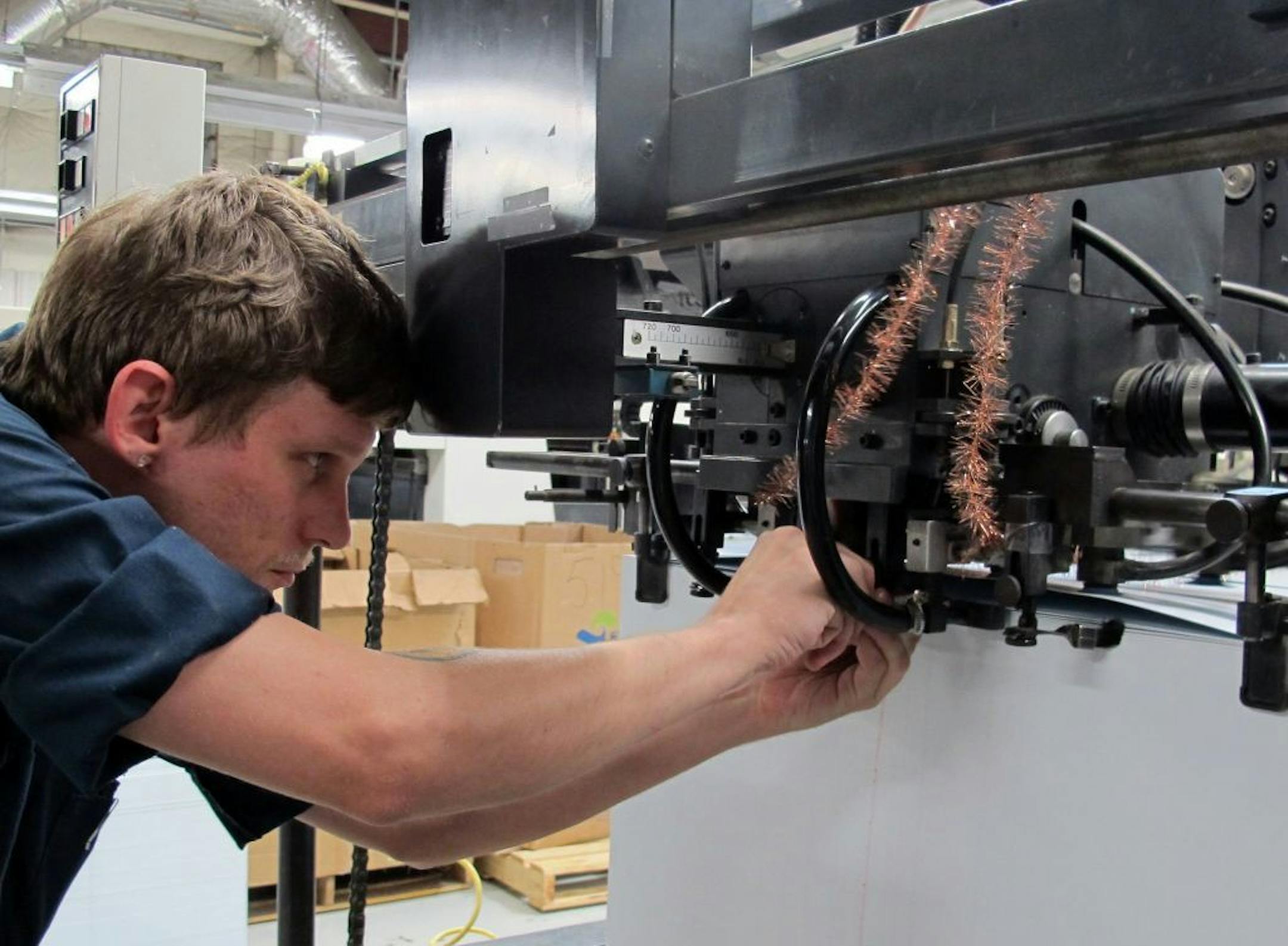 A worker at Plasticard-Locktech International in Asheville, North Carolina, adjusts machinery settings at plant where printed magnetic plastic cards are made. The company has become a formidable exporter of hotel key cards and gift cards.