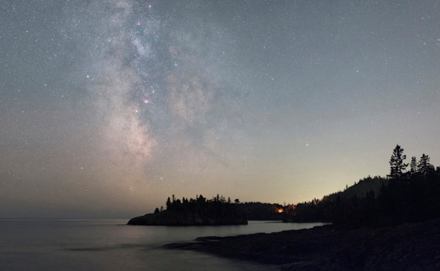 ONE TIME USE. Camping in Minnesota's state parks is a great way to observe the Milky Way and its night sky treasures. Their dark skies give you some of the best observing possibilities in the state. In this scene from Split Rock Lighthouse State Park, you can find the sparkling galactic core region of the Milky Way poised over Ellingson Island in Lake Superior, as well as a late night campfire glowing in the trees. See if you can find the four pinkish objects arranged vertically along the middle of the Milky Way. They are the Eagle, Omega, Trifid and Lagoon nebulae, from top to bottom.