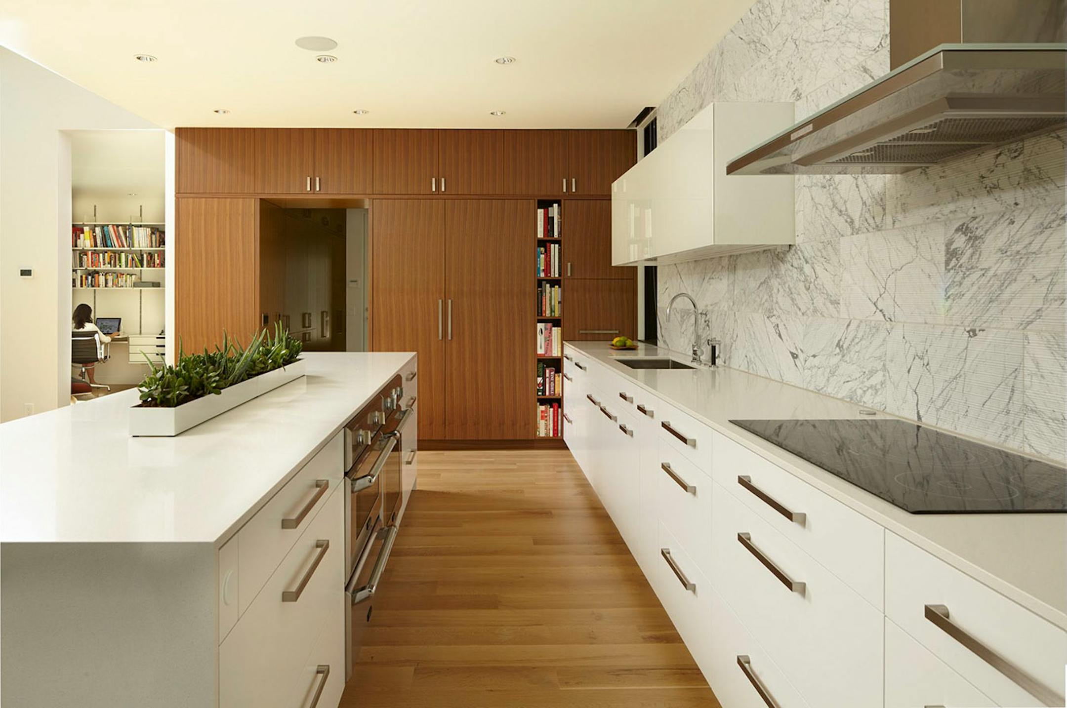 A wall of walnut cabinets adds more storage and warms up the white and gray kitchen.