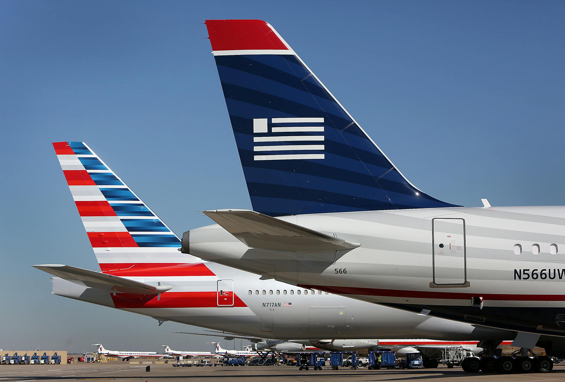An AMR Corp.'s American Airlines airplane, left, and a US Airways Group Inc. airplane sit parked at a gate at Dallas Fort Worth Airport in Fort Worth, Texas, U.S., on Thursday, Feb. 14, 2013. US Airways Group Inc., spurned in three prior merger attempts, will combine with bankrupt AMR Corp.�s American Airlines in an $11 billion all-stock deal to create the world�s largest carrier. Photographer: Mike Fuentes/Bloomberg
