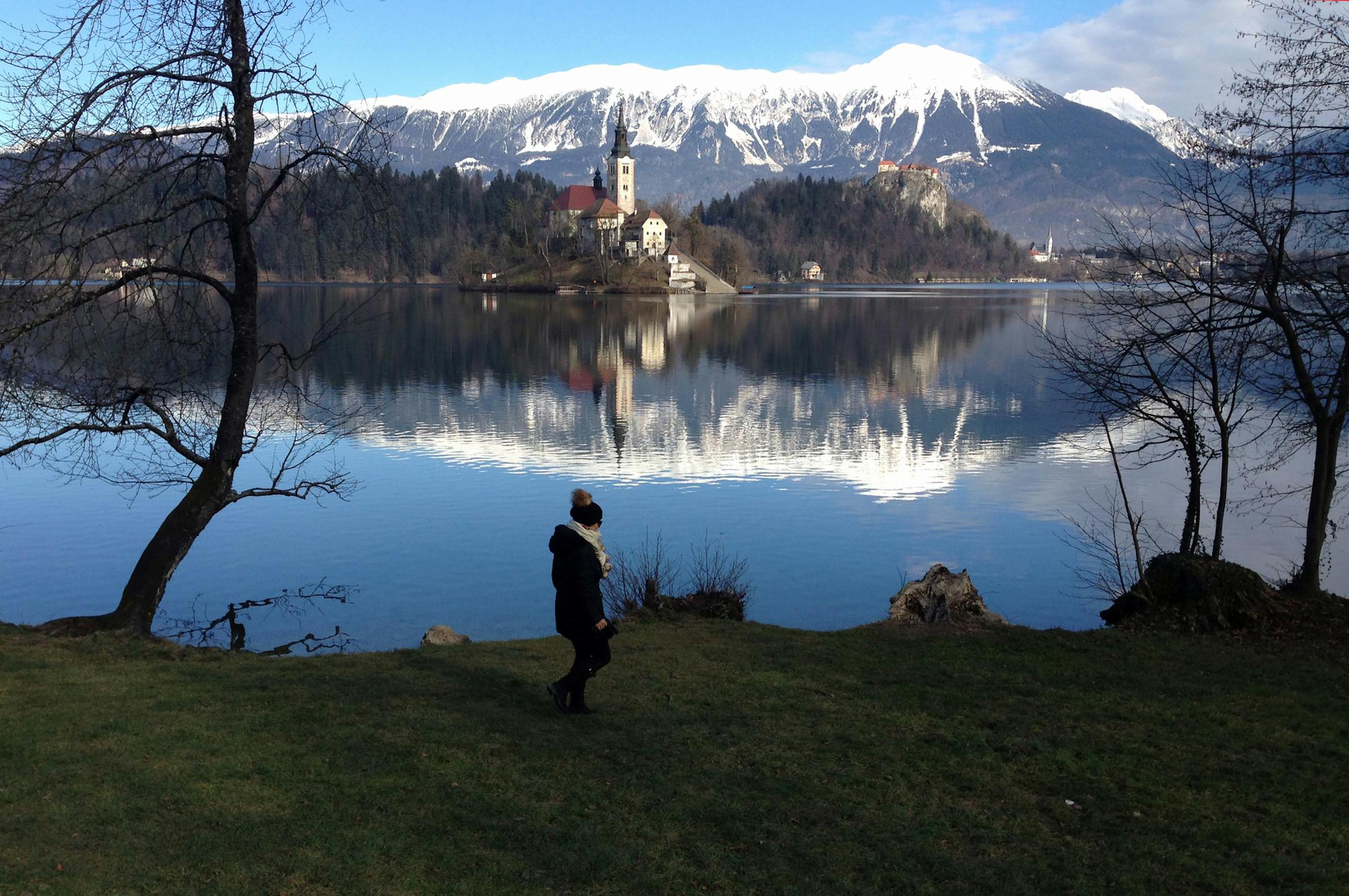 CORRECTS THE LOCATION OF THE LAKE In this photo taken Tuesday, Jan. 27, 2015, a woman walks by the Lake Bled in Slovenia with a island and the Church of Our Lady on it. Tucked in the northwestern corner of Slovenia, between Austria and Italy, stands a spectacular landscape: a lush tiny island in the middle of the emerald-green lake waters, with a church tower peeking out of the evergreens, surrounded by snow-covered rocky Alps. (AP Photo/Dusan Stojanovic) ORG XMIT: XDMV504