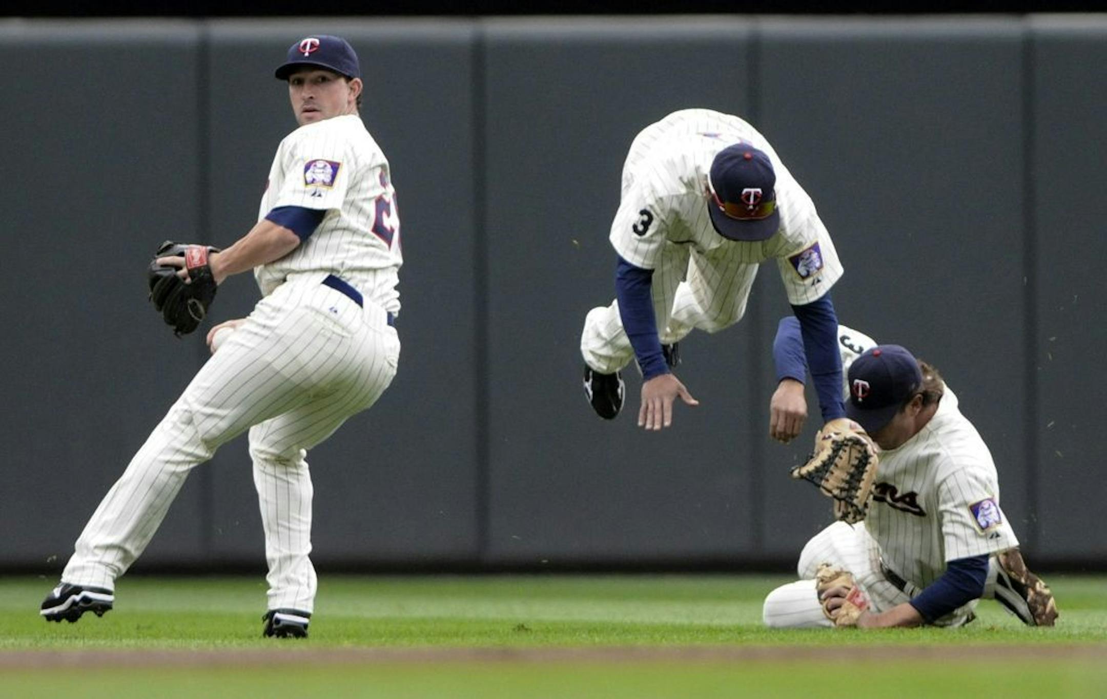 Minnesota's Ben Revere, center, flies over shortstop Trevor Plouffe as second baseman Brian Dinkelman prepares to throw after the three converged unsuccessfully on a shallow pop fly for an RBI single by Seattle's Justin Smoak in the first inning Thursday.