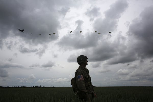 A WWII enthusiast watches French and British parachutists jumping during a commemorative parachute jump over Sannerville, Normandy, Wednesday.