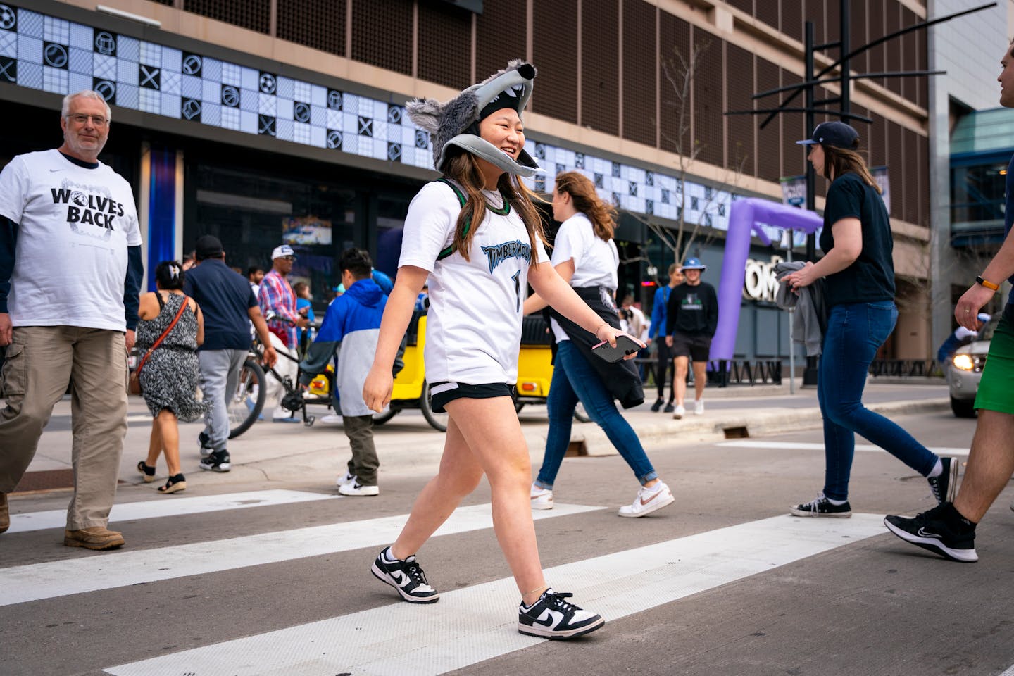 Grace Dvorak, in a Crunch the Wolf hat mask, crosses the street as she joins fans heading to the Timberwolves playoff game against the Denver Nuggets 