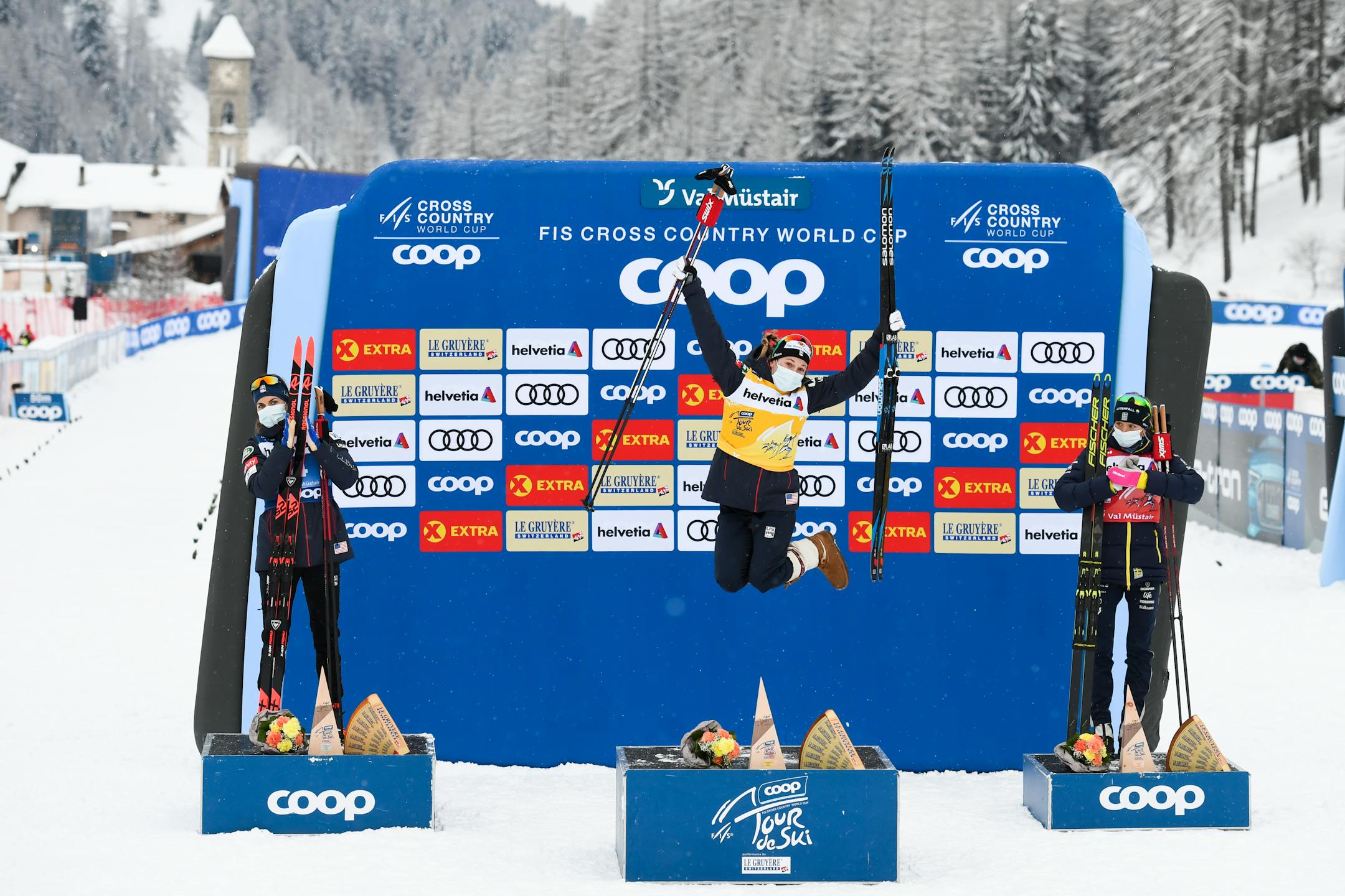 Winner Jessie Diggins of the USA celebrates on the podium with second place Rosie Brennan of USA, left, and third place Frida Karlsson of Sweden after the women's 10km free style pursuit race of the Tour de Ski, in Tschierv, Switzerland