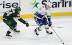 Vancouver Canucks Ben Hutton (27) controls the puck in front of Minnesota Wild's Mikael Granlund (64) in the first period of an NHL hockey game Sunday
