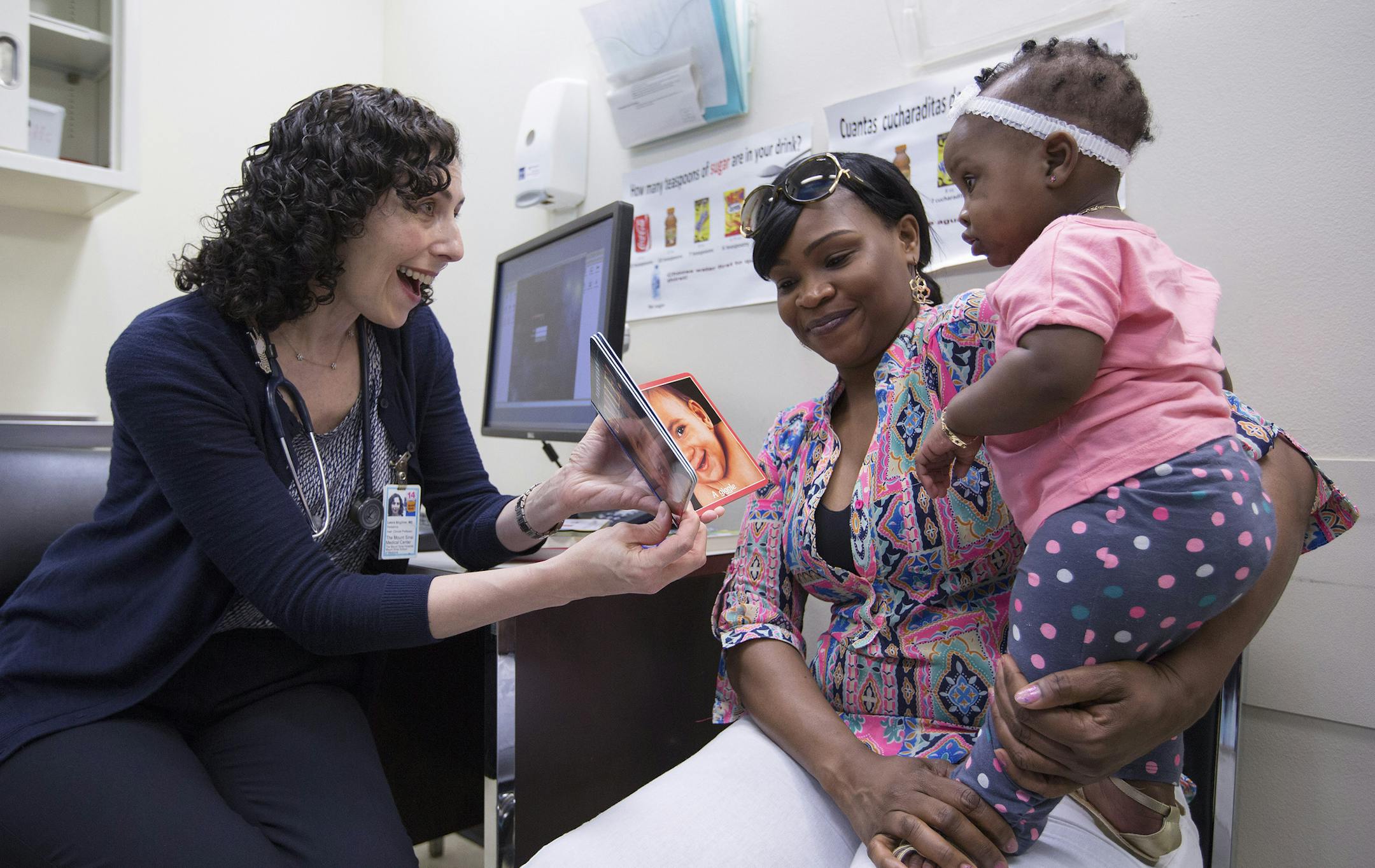 **EMBARGO: No electronic distribution, Web posting or street sales before Tuesday 12:01 a.m. ET June 24, 2014. No exceptions for any reasons. EMBARGO set by source.** Dr. Leora Mogilner shows a book to nine-month old Kaylee Smith and her mother, Tameka Griffiths, at Mount Sinai Hospital in New York, June 23, 2014. Stressing the importance of a brain development over an infant's first 1,000 days, the American Academy of Pediatrics has issued new guidelines calling on members to urge parents to be