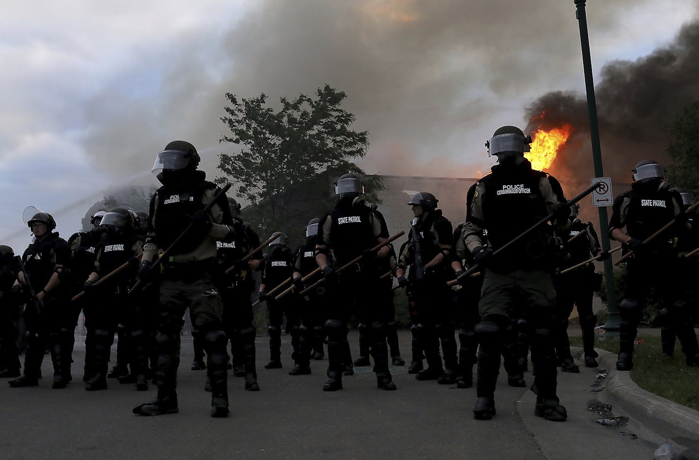 Law enforcement officers amass to protect nearby firefighters as a blaze burns along Lake St., near the Minneapolis police 3rd precinct, after a night of unrest and protests in the death of George Floyd early Friday, May 29, 2020 in Minneapolis. Floyd died after being restrained by Minneapolis police officers on Memorial Day. (David Joles/Star Tribune via AP)