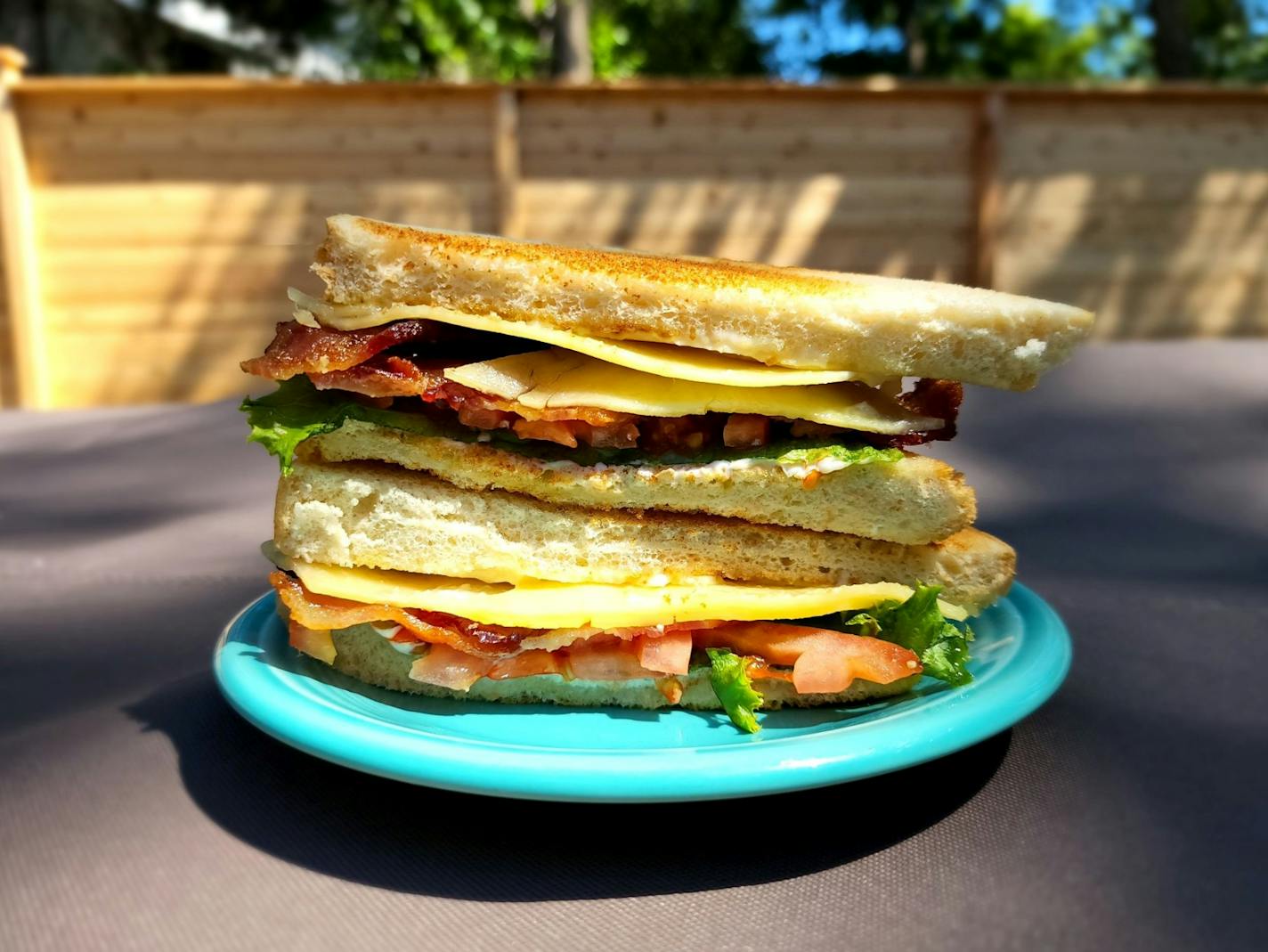 Two halves of a BLT sandwich stacked on a plate, shot outdoors.