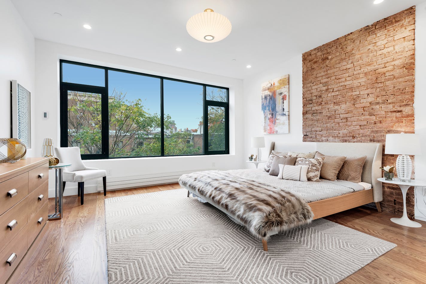 A large bed with no footboard with a faux fur throw over the end and a half dozen neutral-colored pillows arranged at the headboard.