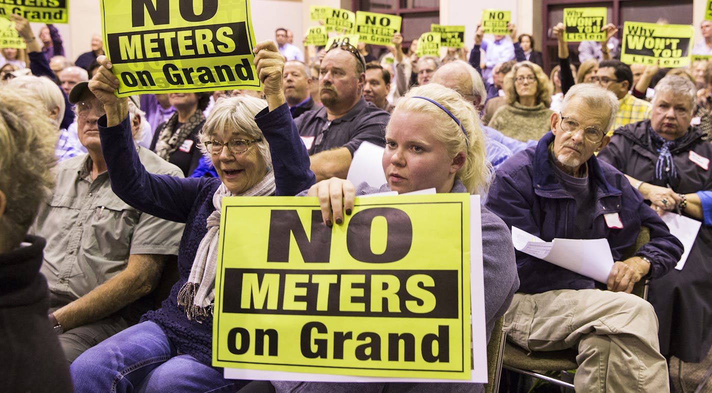 People opposed to parking meters on Grand Avenue, including Kerry O'Keefe, center, who lives on Grand Avenue, hold up signs during a public meeting with St. Paul Mayor Chris Coleman at William Mitchell College of Law in St. Paul on Monday, October 19, 2015.