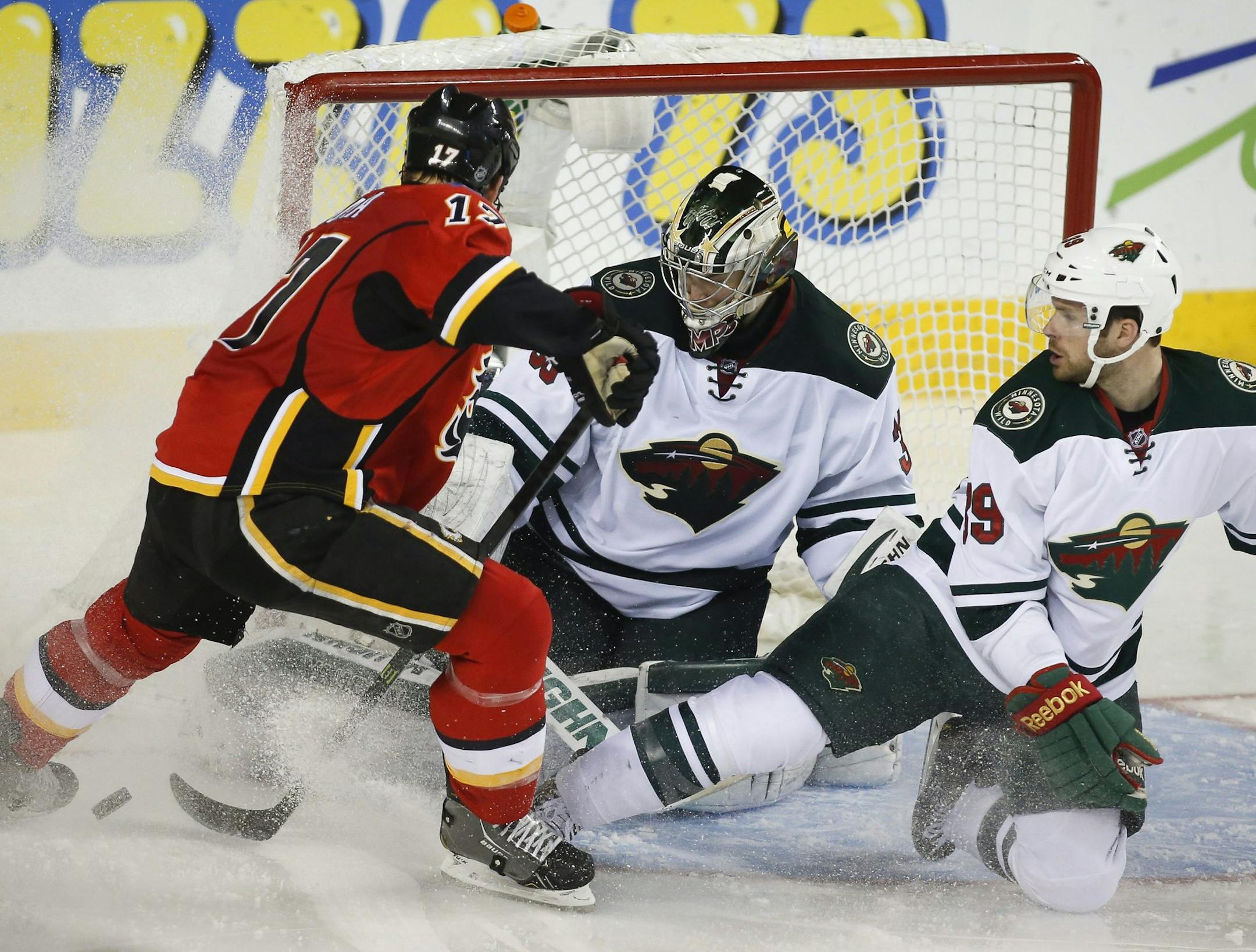 Minnesota Wild goalie Darcy Kuemper, center, kicks the puck away from Calgary Flames' Lance Bouma, left, with the help of teammate Nate Prosser during the second period of an NHL hockey game in Calgary, Alberta, Saturday, Feb. 1, 2014. (AP Photo/The Canadian Press, Jeff McIntosh)