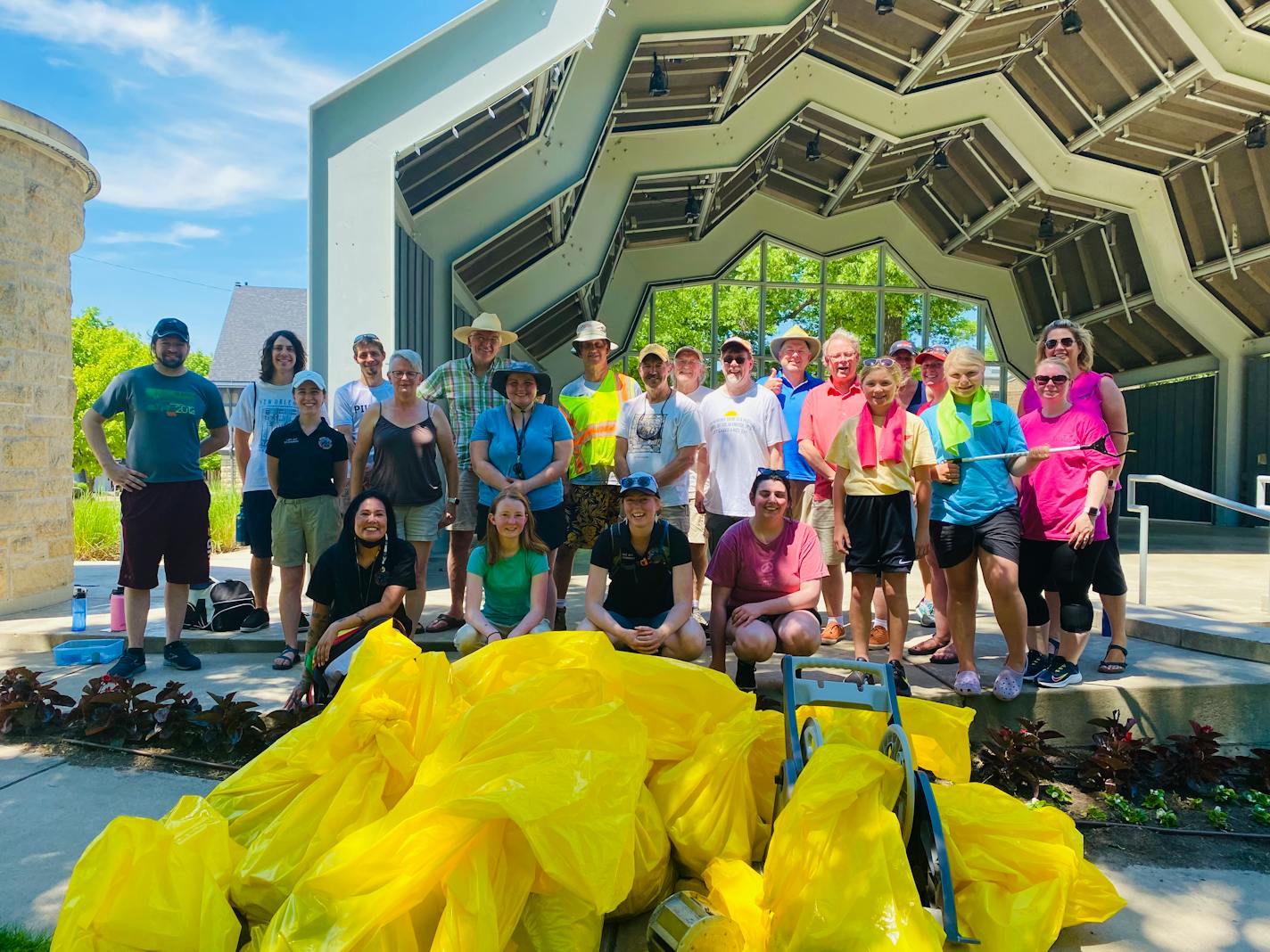 Two dozen smiling volunteers pose in front of bright yellow trash bags, full of litter they collected along the Mississippi River in Goodhue County.