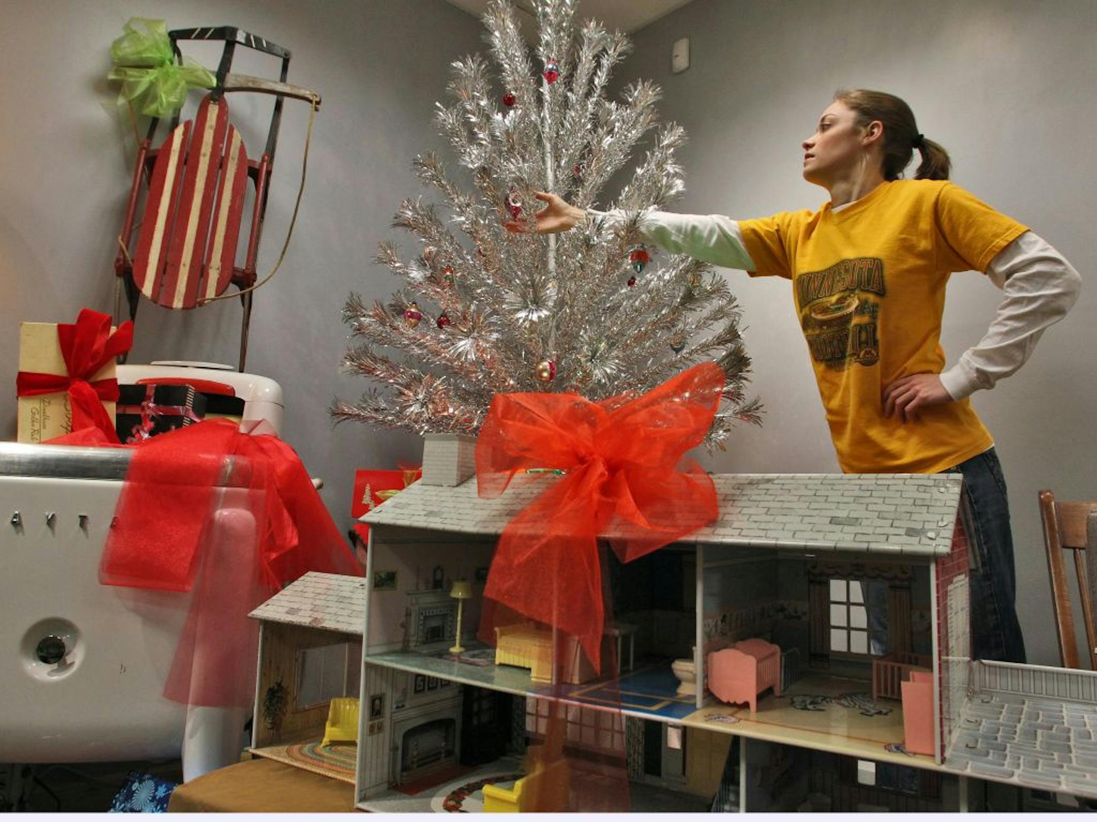 The Richfield Historical Society has decorated a room in their Richfield location with items the way Christmas would have looked in the 1950's. Historical Society intern Karie Ouellette made adjustments on a silver sparkler pom-pom tree. At left, a steel-runner sled sat atop a Maytag wash machine, while a metal doll house is in the foreground.(MARLIN LEVISON/STARTRIBUNE(mlevison@startribune.com