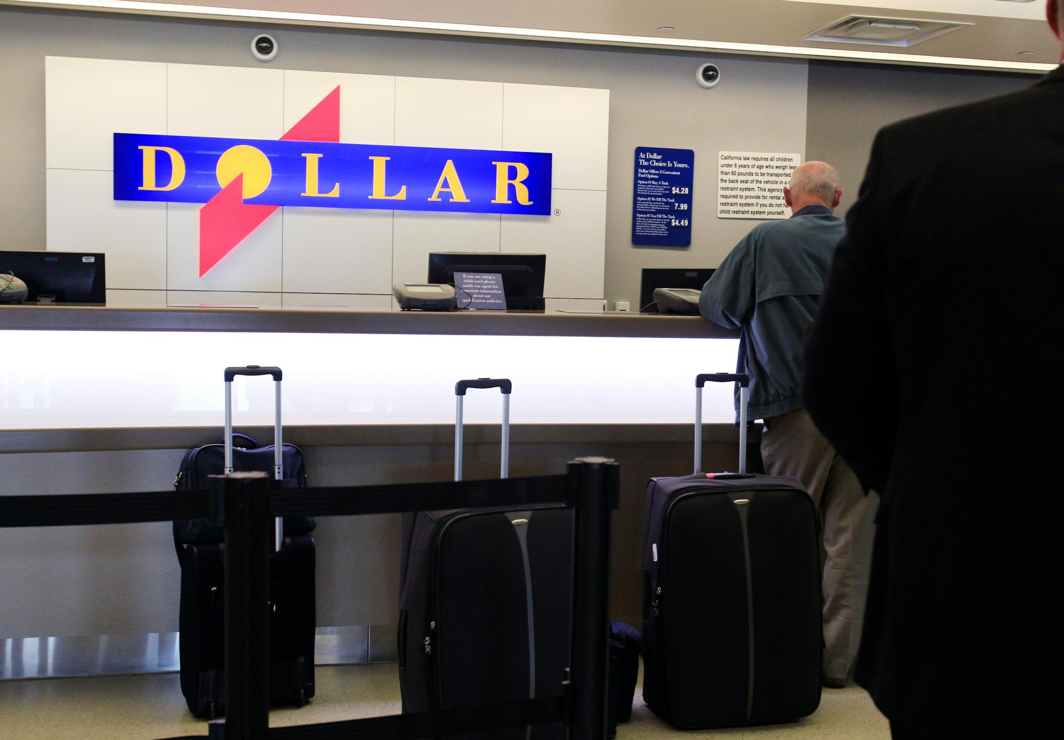 FILE - In this May 9, 2011 file photo, customers wait in line at a Dollar rental car counter at San Jose International Airport in San Jose, Calif. More than two years after its original bid, Hertz agreed Sunday, Aug. 26, 2012, to buy Dollar Thrifty Automotive Group Inc. for about $2.3 billion, giving it more ways to attract travelers and expand its international presence. It will also give the company a leg up against competition from an increasing number of smaller competitors. (AP Photo/Paul Sakuma, File)