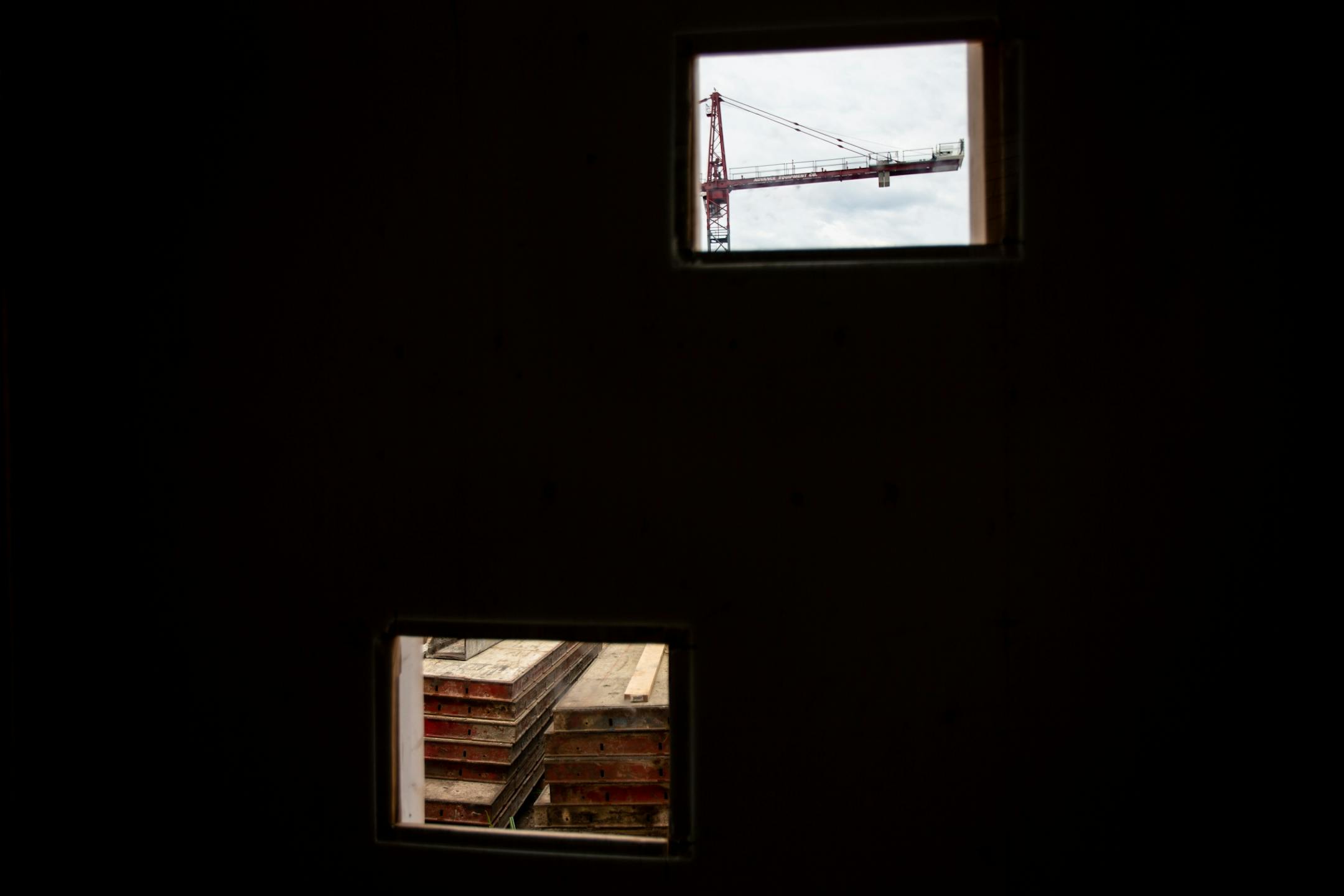 A crane and building materials can be seen through some openings in a temporary wall meant to block pedestrian view of the unsightly construction.